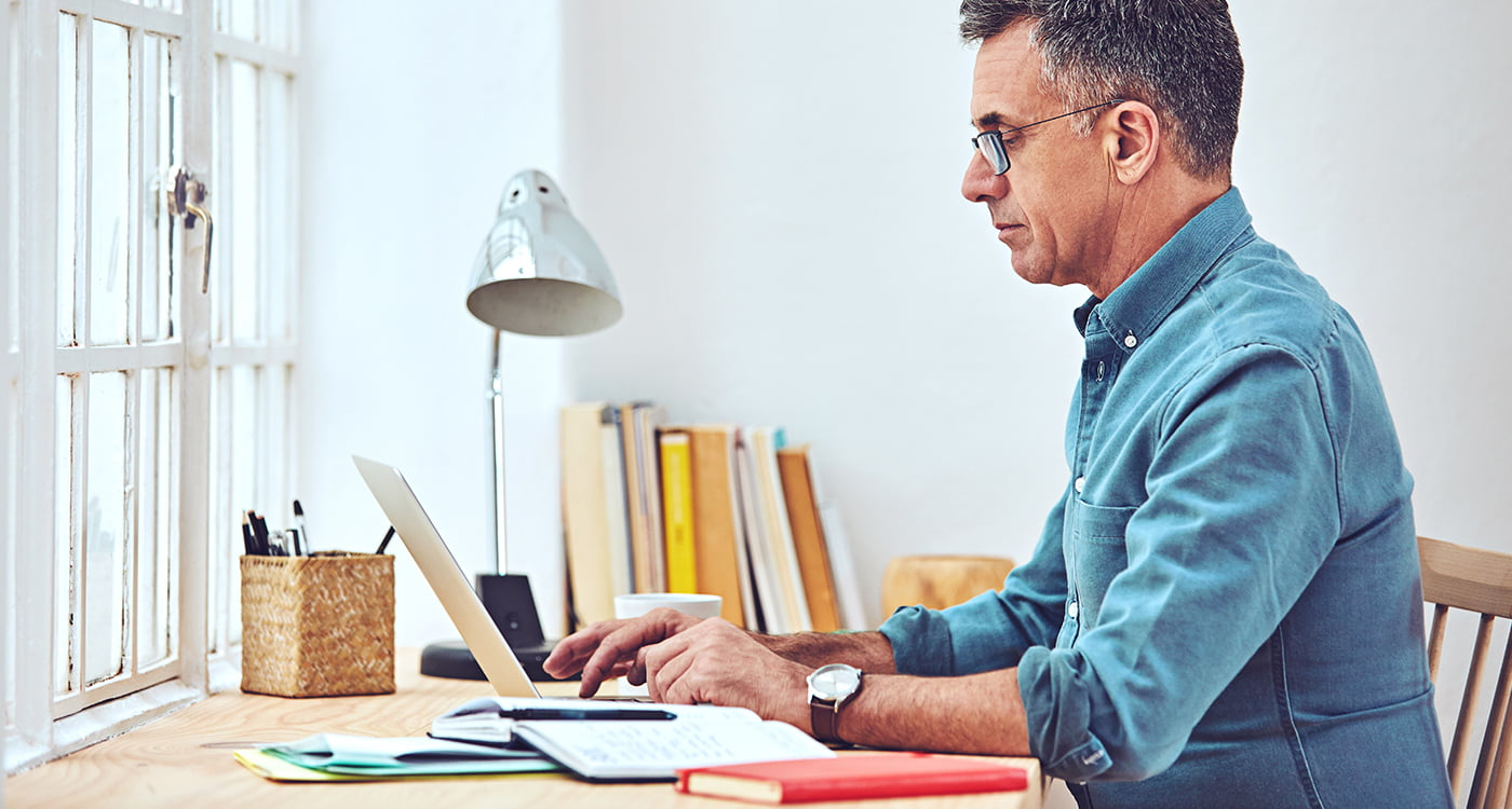 a man sitting as his desk working on his laptop